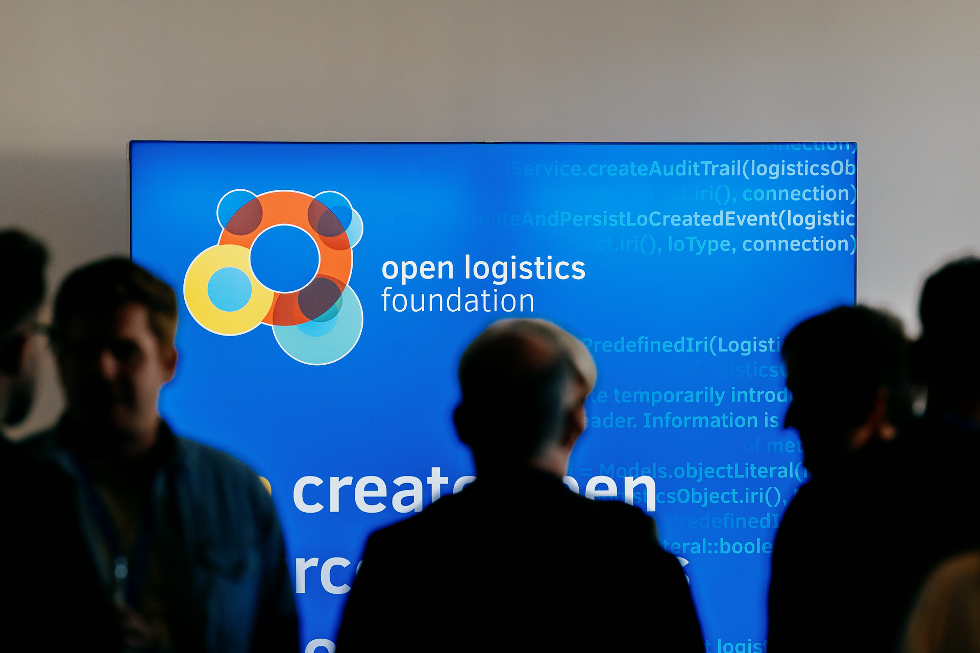 Attendees silhouetted in front of a screen showing the Open Logistics Foundation logo at a Foundation event